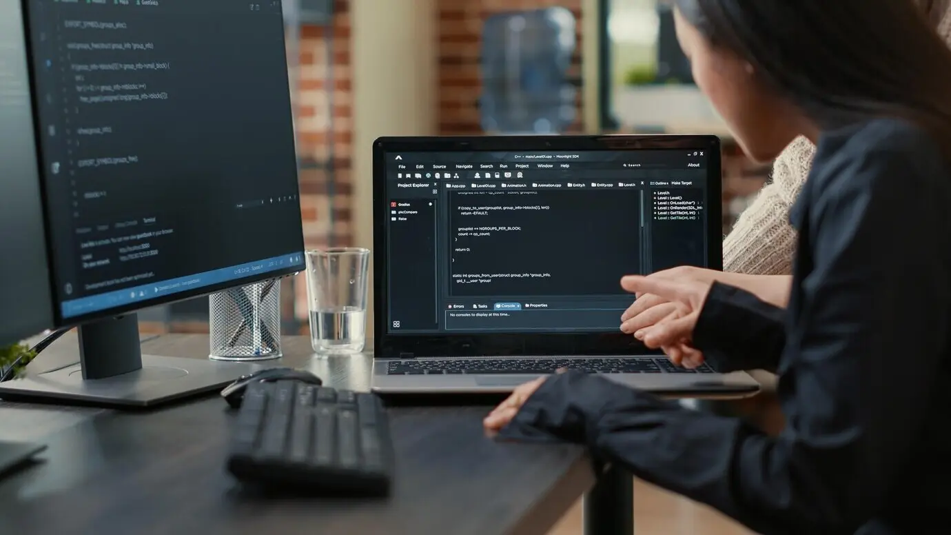 Ein Team von Programmierern diskutiert einen auf dem Laptopbildschirm laufenden Algorithmus und zeigt dabei auf den Quellcode, während sie am Schreibtisch sitzen. Softwareentwickler arbeiten gemeinsam an einem Gruppenprojekt zur Datenkodierung.